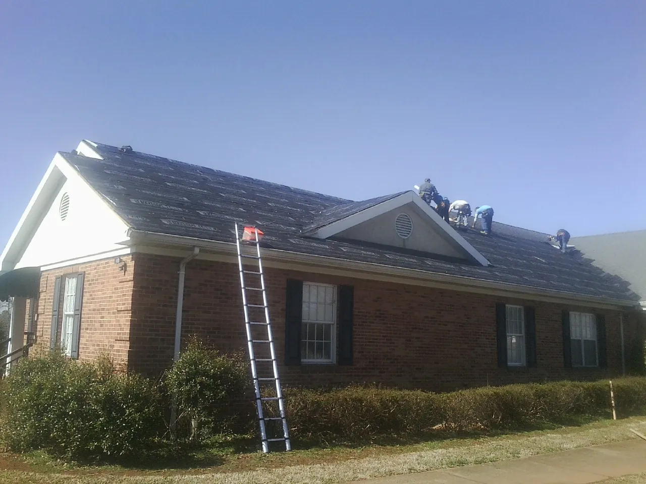 Crew tearing shingles off a brick ranch roof with a ladder set — Emergency Roof Repair work by our crew in Central Bridge