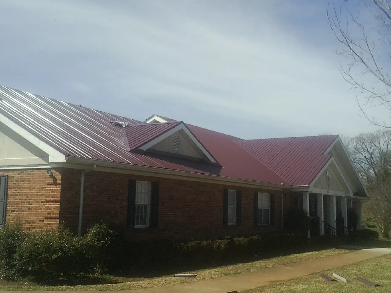 Red metal roof with gabled entries on a long brick building, from a Hail Damage Roof Repair job in Central Bridge