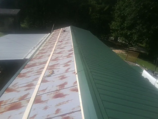 Old rusted panels beside newly installed green metal roofing — Wind Damage Roof Repair by Roofing Brothers in Central Bridge
