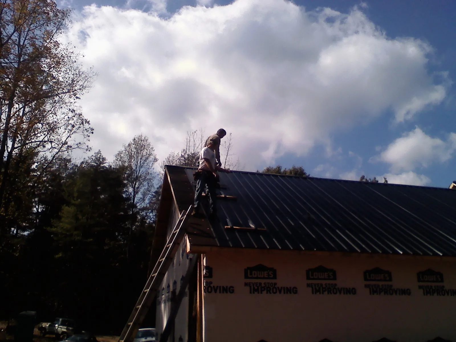 Roofer fastening dark metal panels high against a cloudy sky, from a Roof Inspection job in Central Bridge